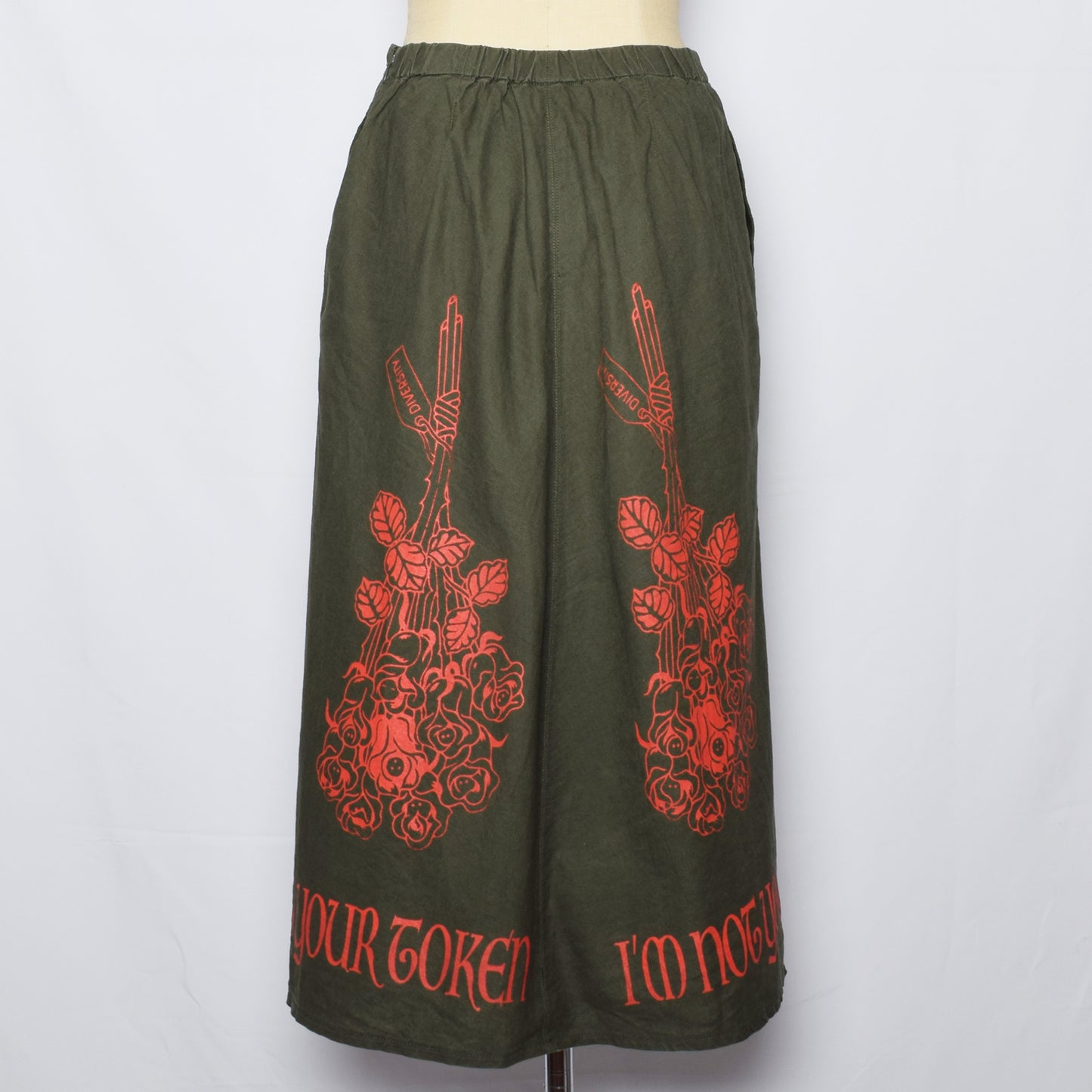 カーキ色のロングスカートに花束に一本だけ違う色の花が混ざったプリントと、裾にI'm not your tokenの文字