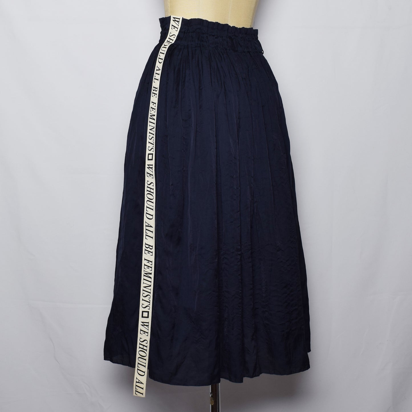 ワッシャー素材のネイビーのスカートのサイドに、We should all be Feministsとプリントされたリボンが縫い付けられている。