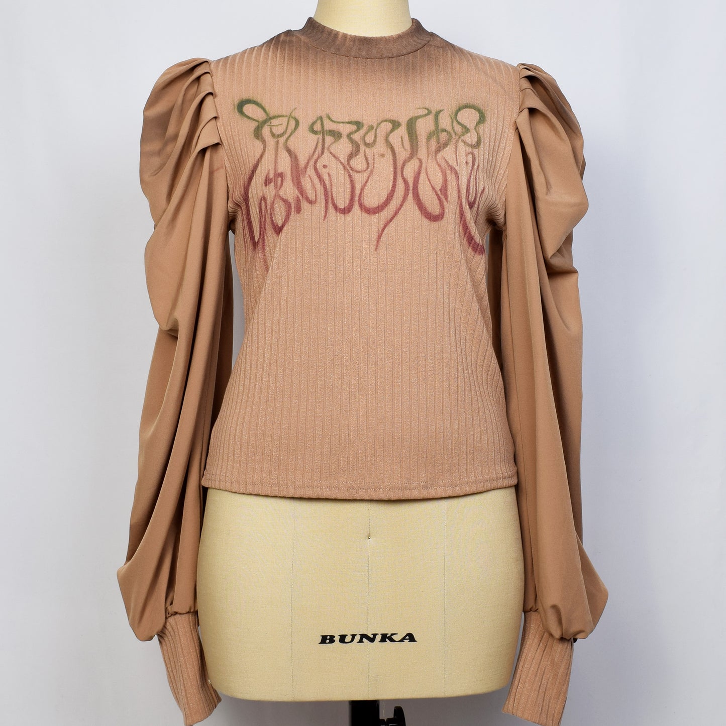 ブラウンのパフスリーブリブニット長袖トップスに崩し文字で基本的人権とプリントされている。