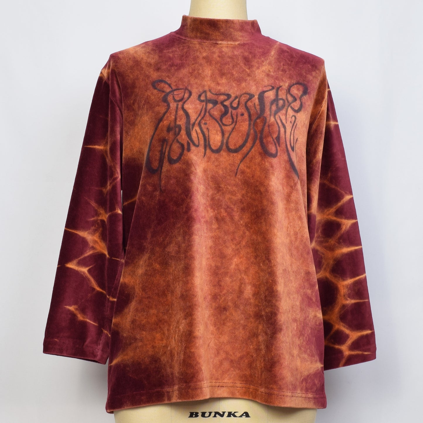 褐色ブラウンのムラ柄ベロア調長袖トップスに崩し文字で基本的人権とプリントされている。