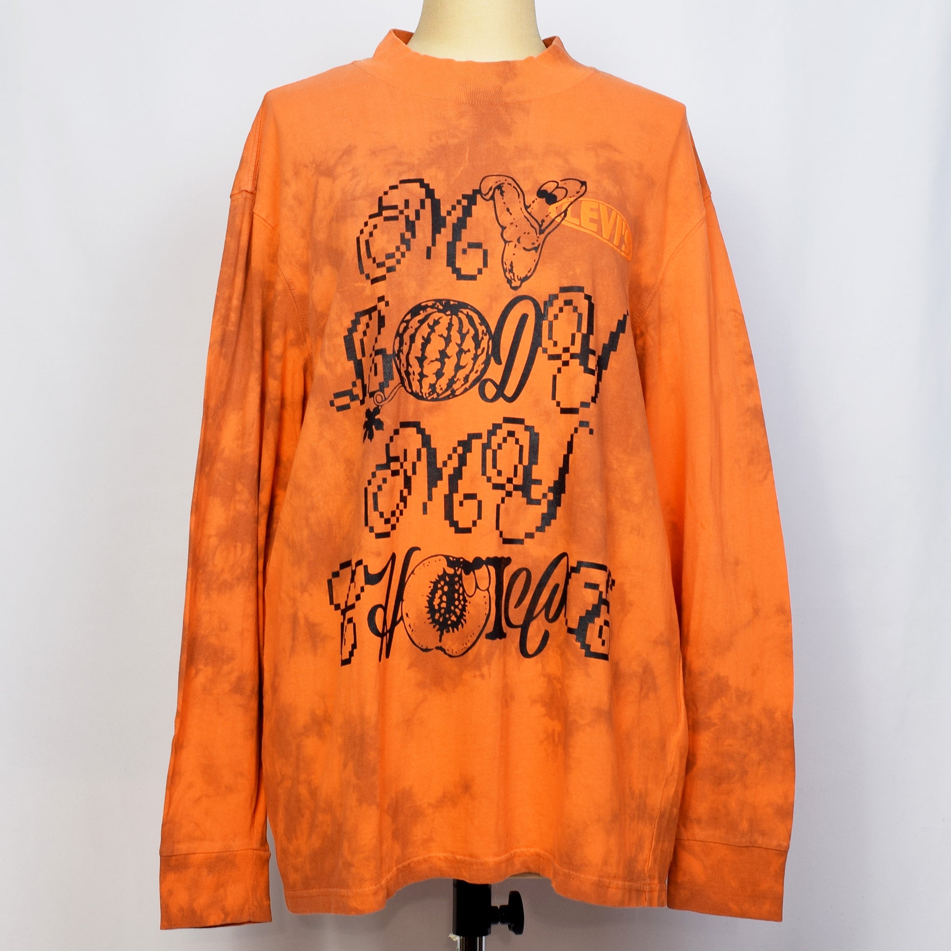 タイダイ柄のオレンジの長袖トップスにMY BODY MY CHOICEとバナナ、プラム、スイカのイラストのプリント。