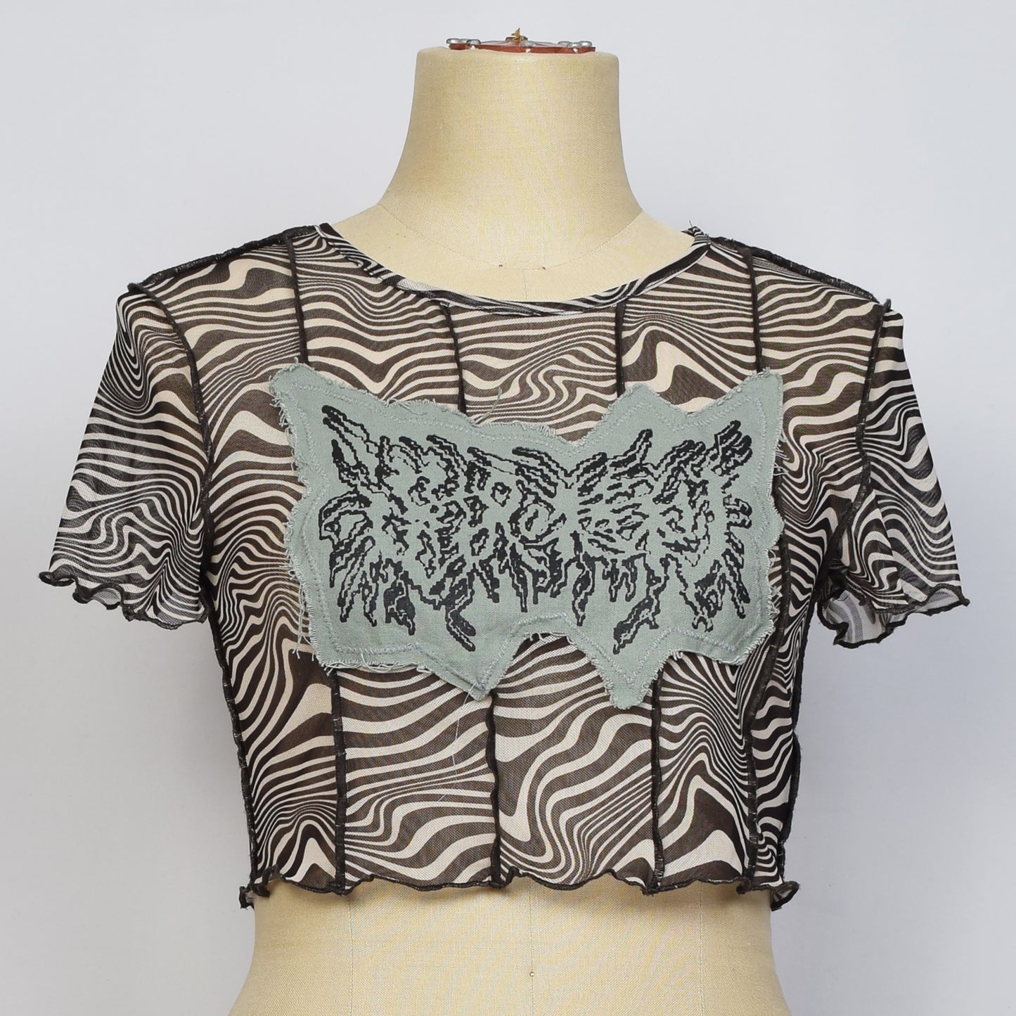 シアー素材のゼブラ柄のマーブル模様の丈の短いトップスにブルーグレーの布が縫い付けられていて、選択の権利という文字がメタルロゴ風にプリントされている。