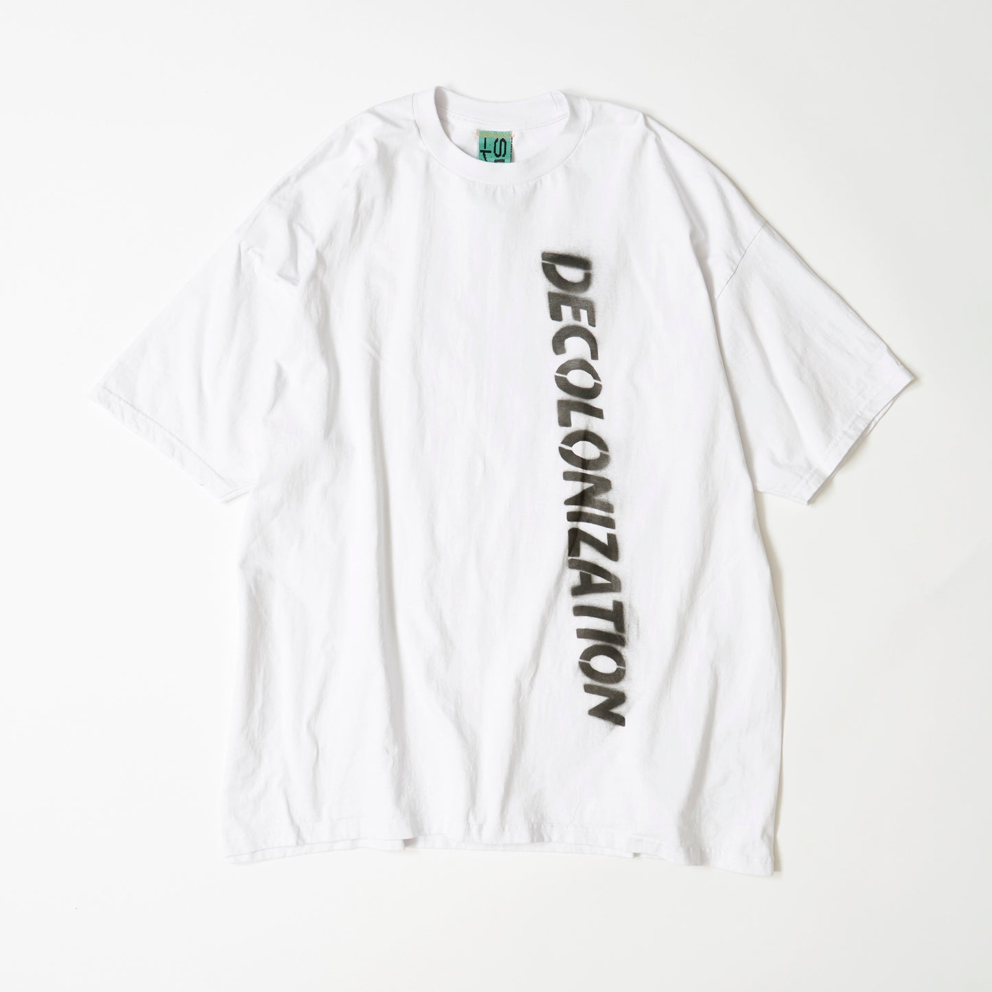 白い大きなTシャツにDECOLONIZATIONの文字が黒いスプレーでペイントされている。素材はコットン100