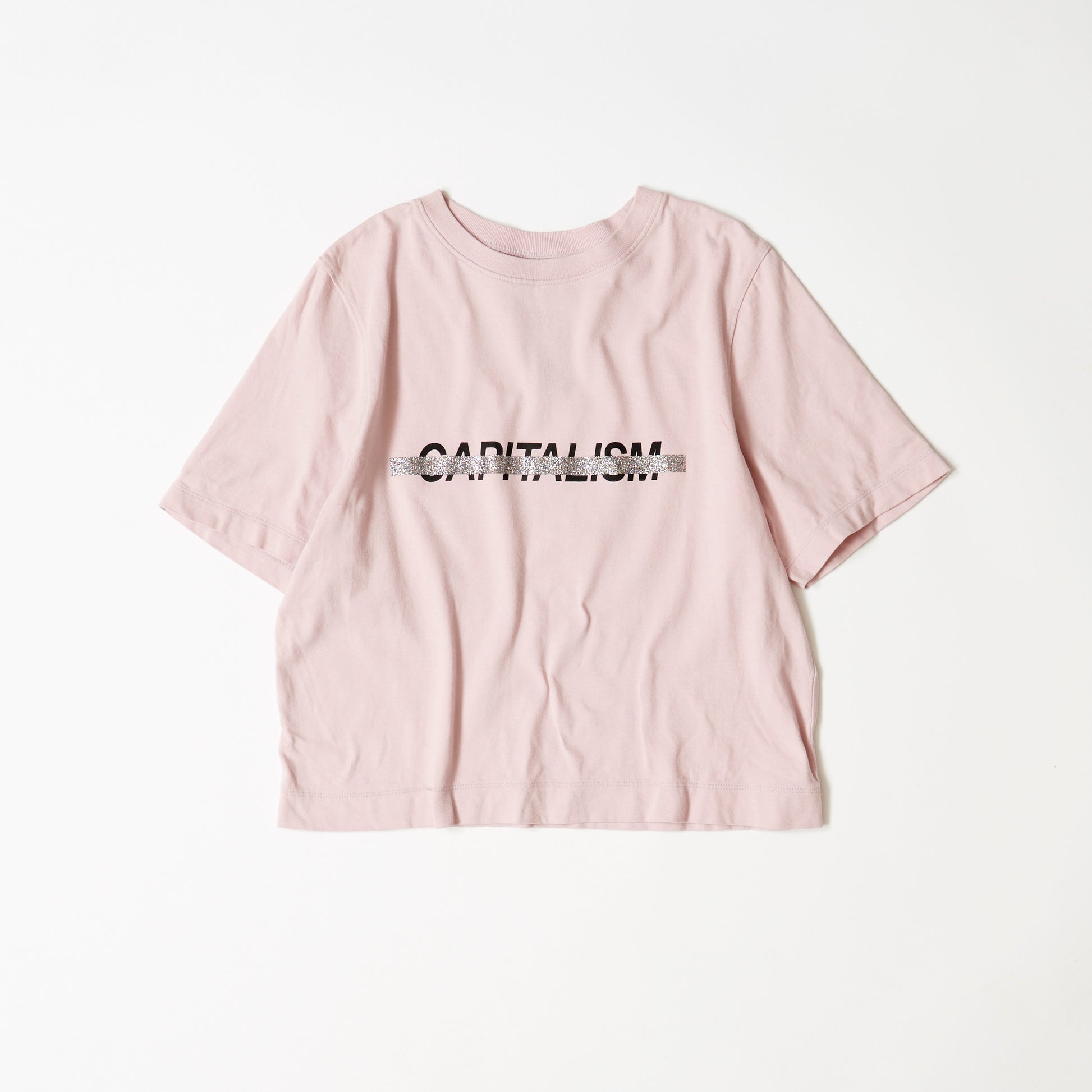 ピンクベージュの半袖TシャツにCAPITALISMの黒いプリントにシルバーのラメで打ち消し線のプリント。表面。コットン１００