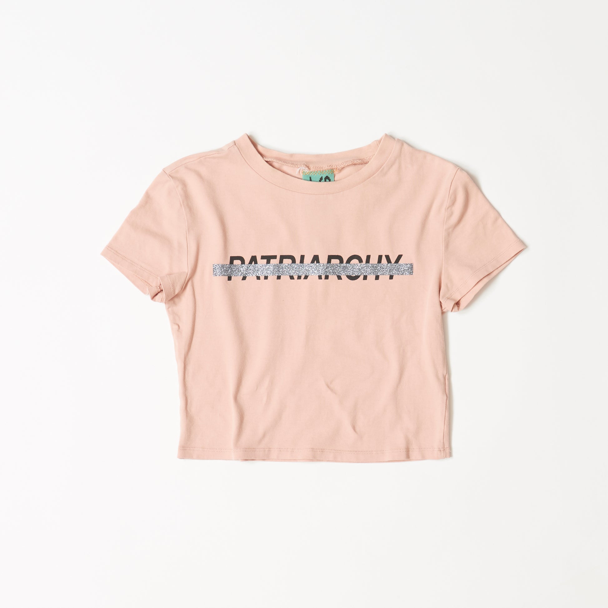 アプリコット色の半袖TシャツにPATRIARCHYの黒いプリントにシルバーのラメで打ち消し線のプリント。表面。コットン１００