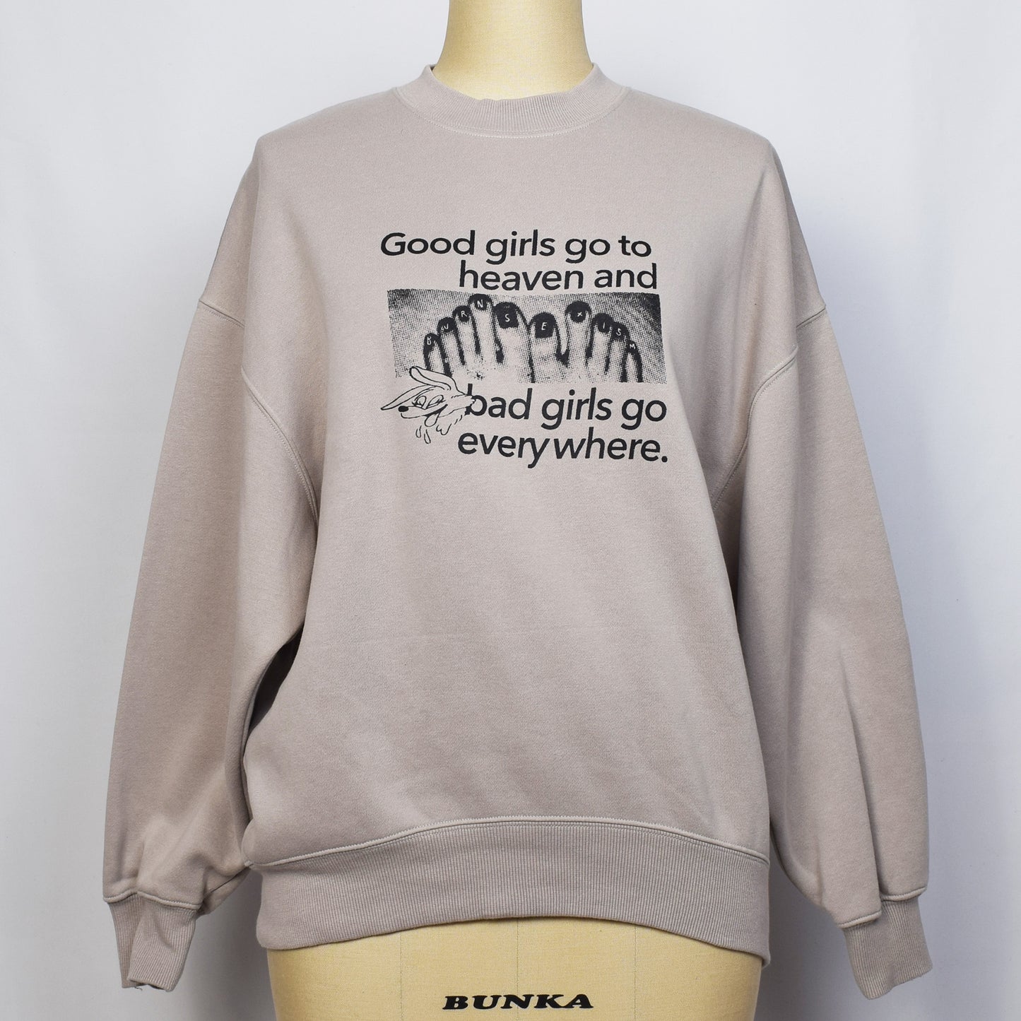 ベージュ色の裏起毛トレーナーにgoodgirl go to heaven badgirl go everywhere と足の写真のグラフィックのプリントがされている。