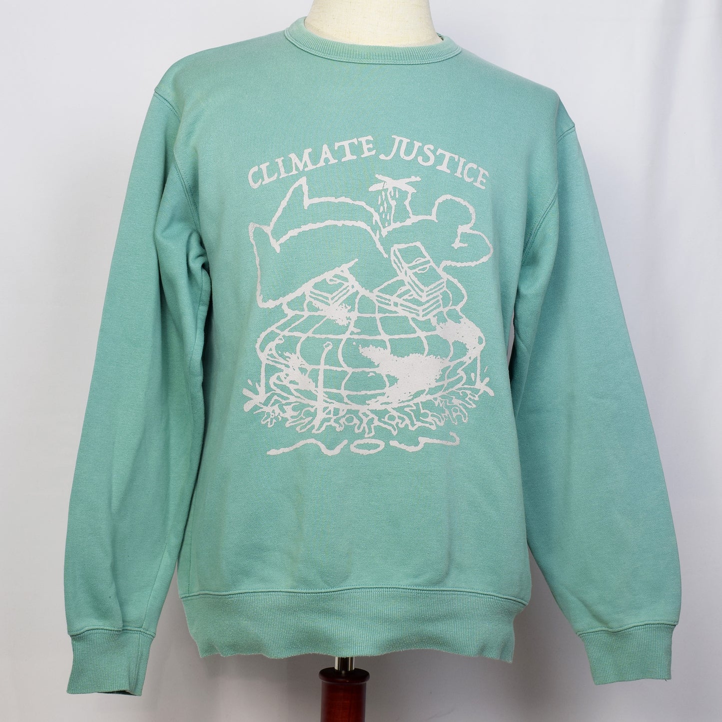 ミントグリーンのトレーナーにClimate Justiceと戦闘機を持った一人の大きい人間と札束が大勢の人と地球を押し潰しているイラストがプリントされている。