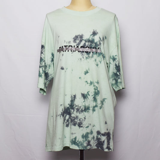 ラベンダー色のタンクトップにPatriarchyのプリントの文字がキラキラのラメのラインで消されている。