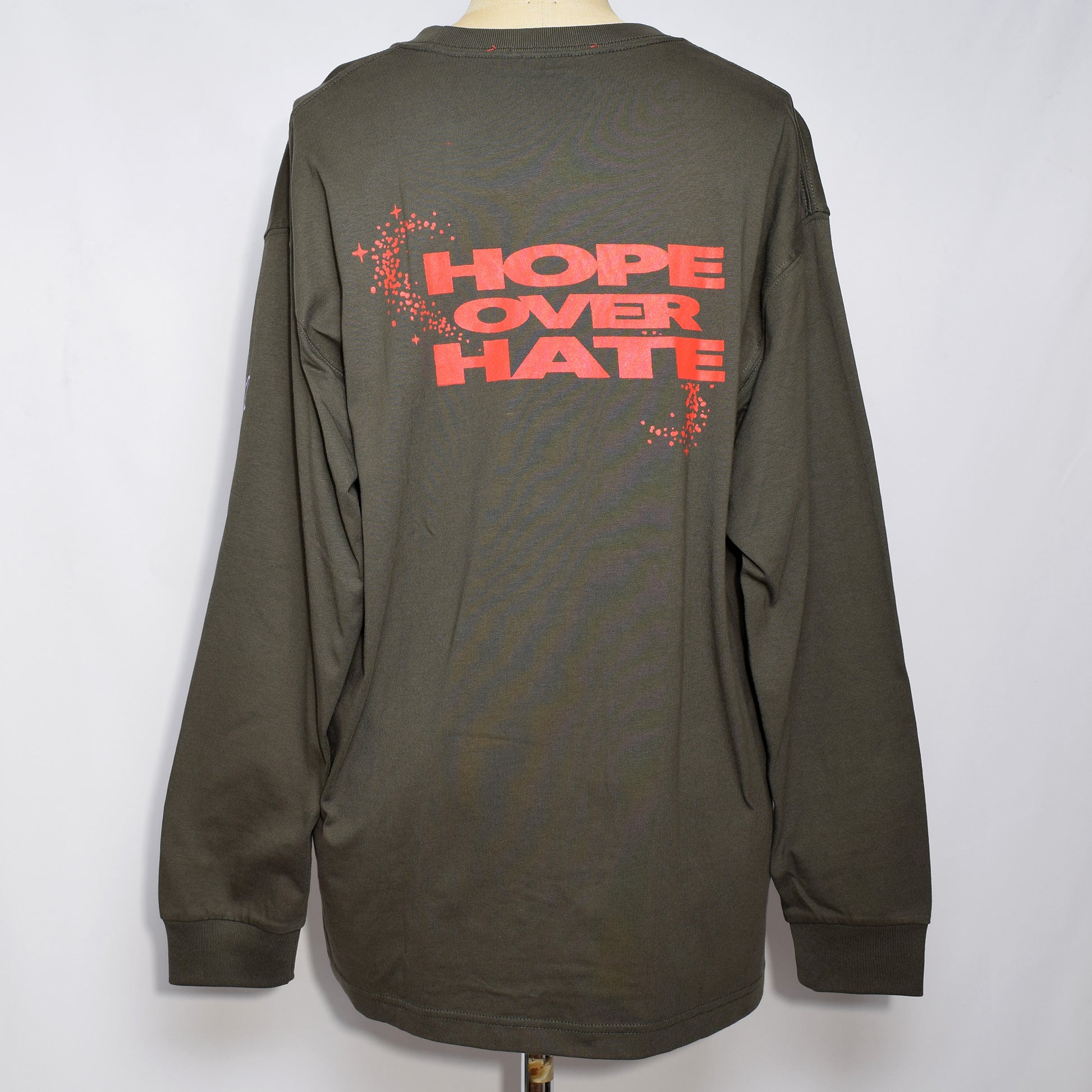 ポケットロングスリーブTシャツ(チャコール色)の背中にHOPE OVER HATEの赤色のプリントと、袖に薄紫の途切れた有刺鉄線のプリント。