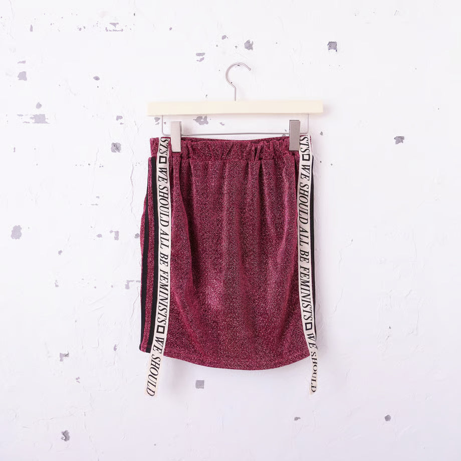 ジャージ素材のキラキラピンクのミニスカートのサイドにWe should all be Feminists と書かれたリボン。