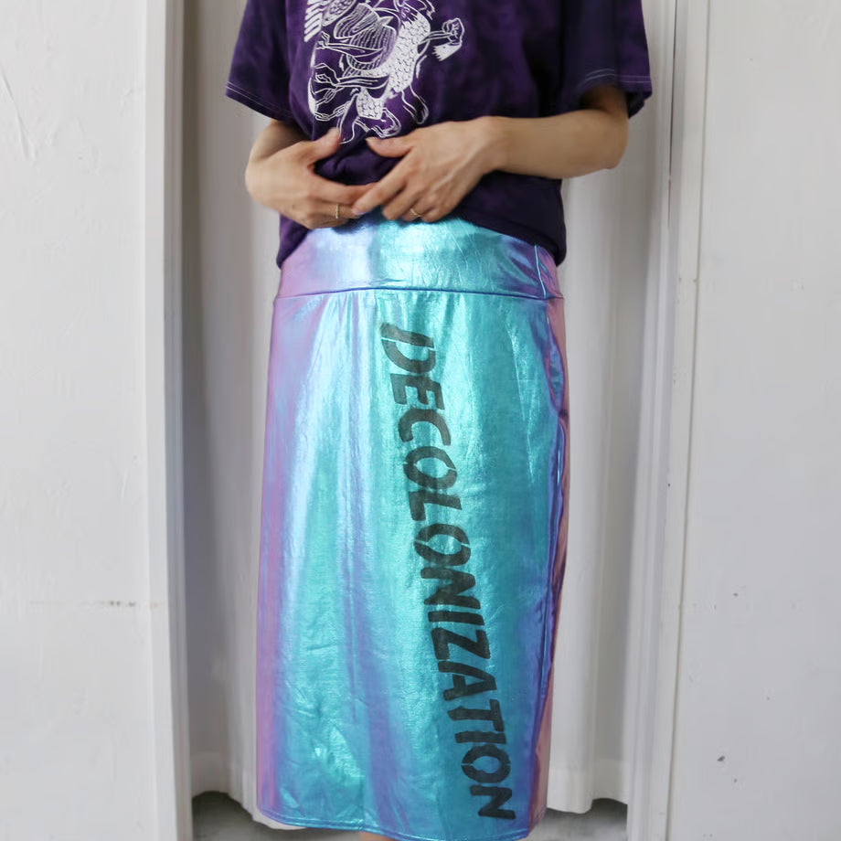 ホログラム色のタイトスカートにQUEER POWERと書かれたハートを抱いたネズミのようなウサギと、DECOLONIZATIONの文字が黒でプリントされている。