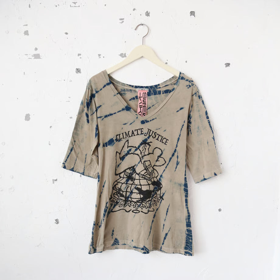 ベージュとネイビーのタイダイ柄Vネック半袖TシャツにCLIMATE JUSTICEの文字と一人の大きな人間と札束に地球と多くの人が押し潰されているグラフィック。