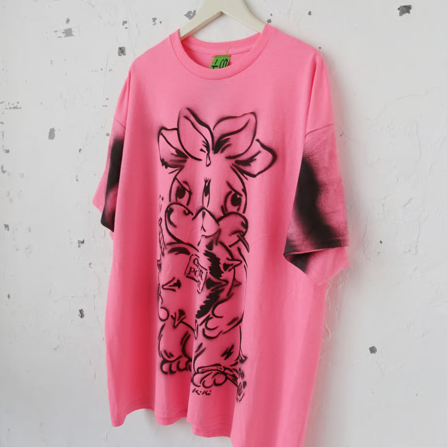 ネオンピンクの大きいサイズのTシャツにQUEER POWER と書かれたハートの爆弾を抱えたネズミのような三つの顔を持ったウサギが大きくスプレーでペイントされている。