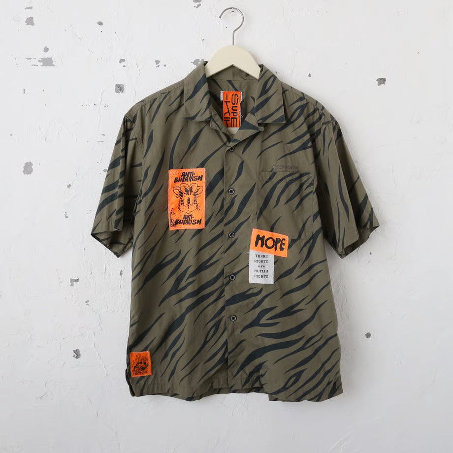 カーキとネイビーのゼブラ柄のシャツにパッチが数枚縫い付けられたリメイクシャツ。