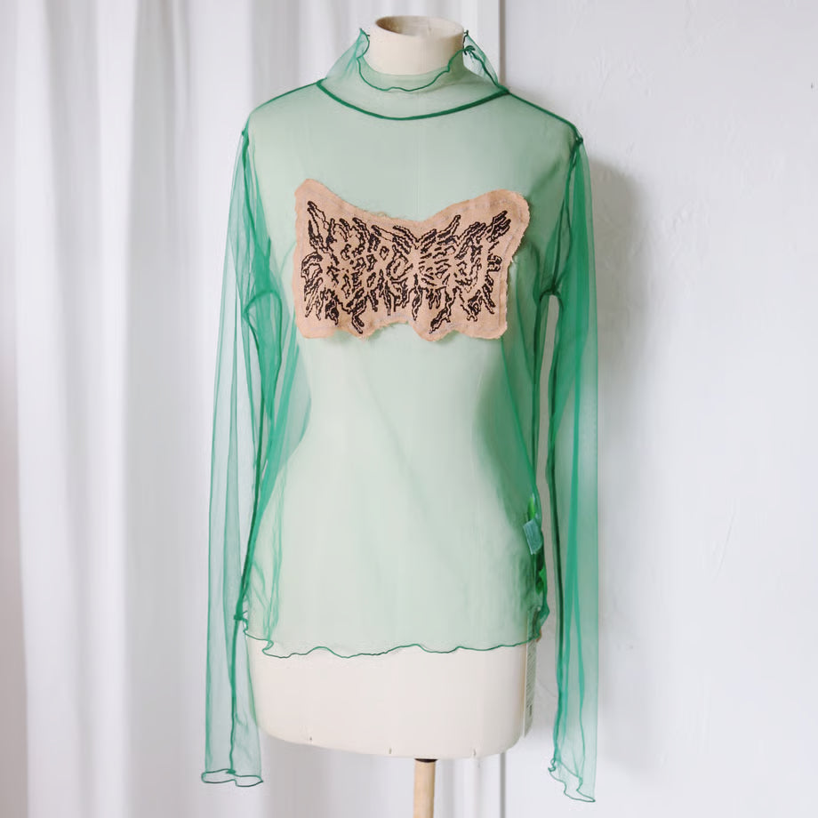 シアー素材のグリーンのロングスリーブトップスに、選択の権利とメタルロゴ風に書かれた布が縫い付けてある。