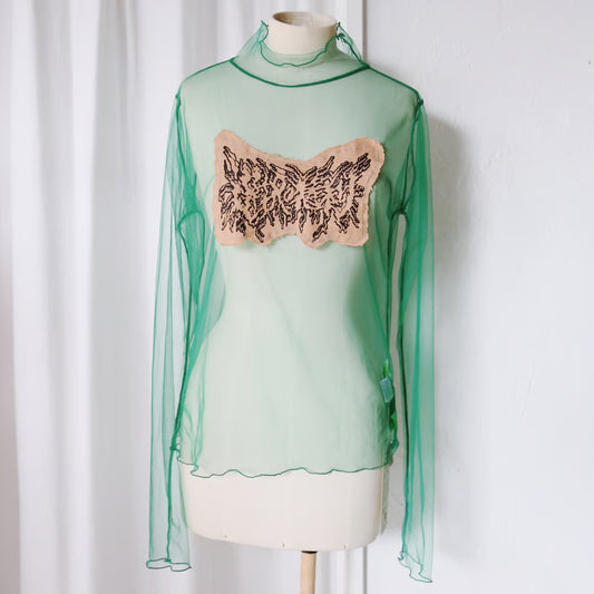 シアー素材のグリーンのロングスリーブトップスに、選択の権利とメタルロゴ風に書かれた布が縫い付けてある。