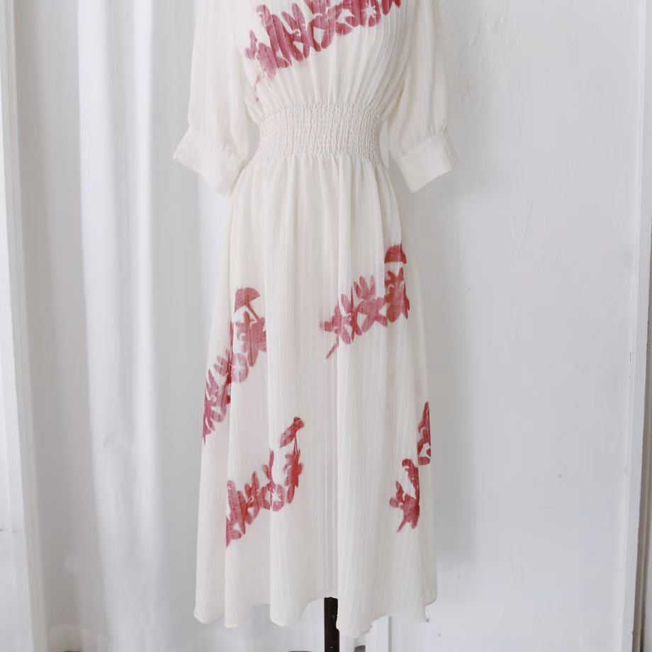 シアー素材のオフホワイトの七分袖のワンピース。謎の動物が手を繋いでいるシルエットのグラフィックが赤い色で数箇所プリントされている。