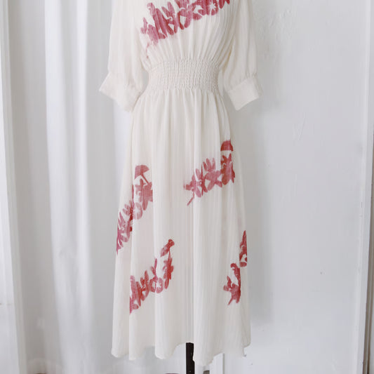 シアー素材のオフホワイトの七分袖のワンピース。謎の動物が手を繋いでいるシルエットのグラフィックが赤い色で数箇所プリントされている。