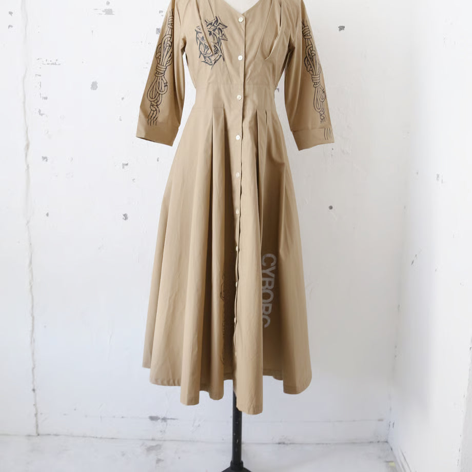 ベージュの長袖の前開きボタンワンピースに、鎖や紐、荊のプリントがされている。