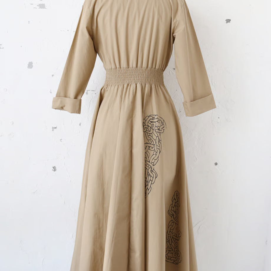 ベージュの長袖の前開きボタンワンピースに、鎖や紐、荊のプリントがされている。