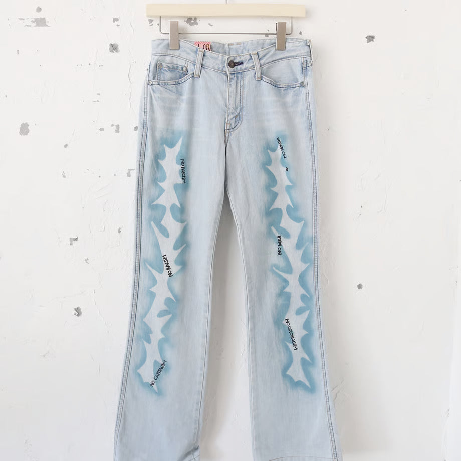 薄い色のデニムパンツに稲妻のようなスプレーペイントと、黒いプリントでno fasism no racism no sexism no colonialism no war　とプリントされている。