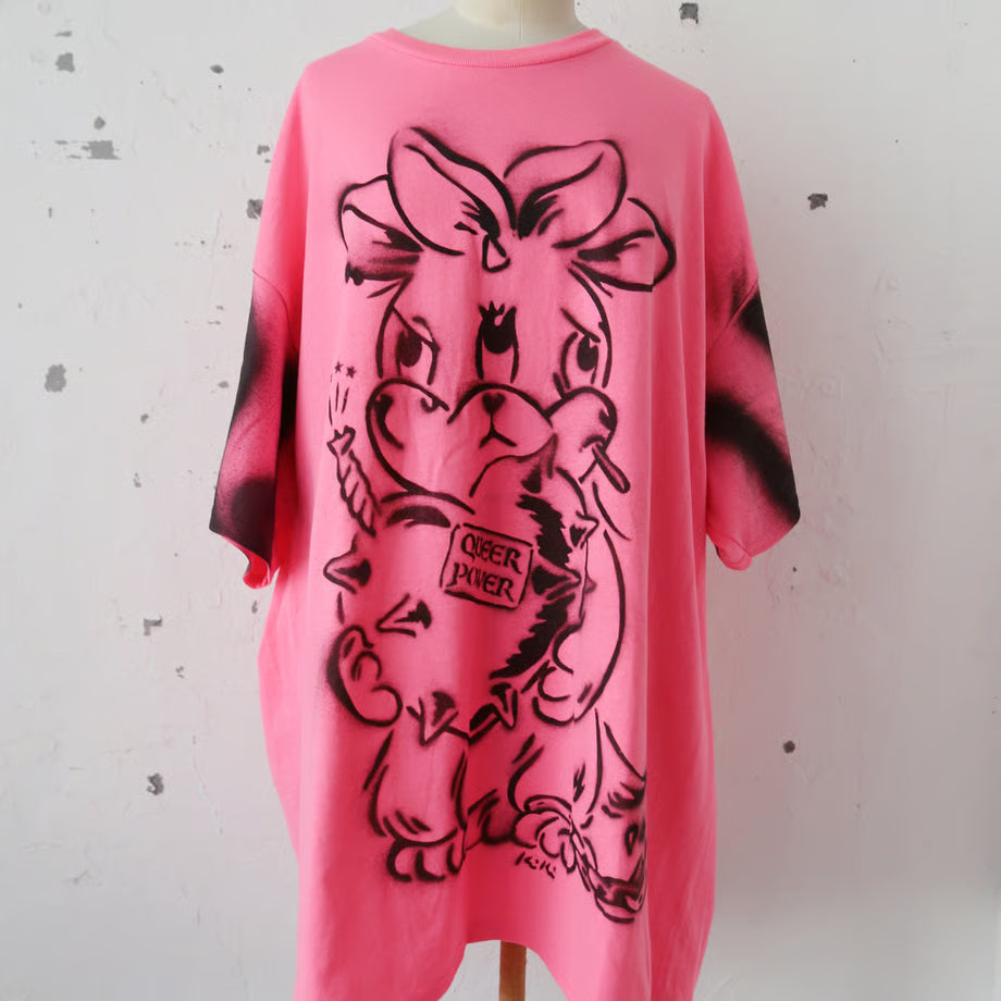 ネオンピンクの大きいサイズのTシャツにQUEER POWER と書かれたハートの爆弾を抱えたネズミのような三つの顔を持ったウサギが大きくスプレーでペイントされている。