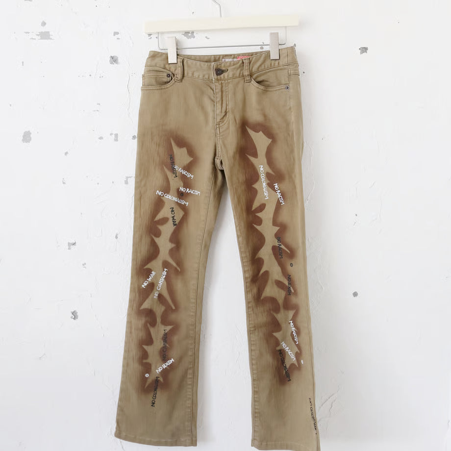薄いブラウンのデニムパンツに稲妻のようなスプレーペイントと、黒いプリントでno fasism no racism no sexism no colonialism no war　とプリントされている。