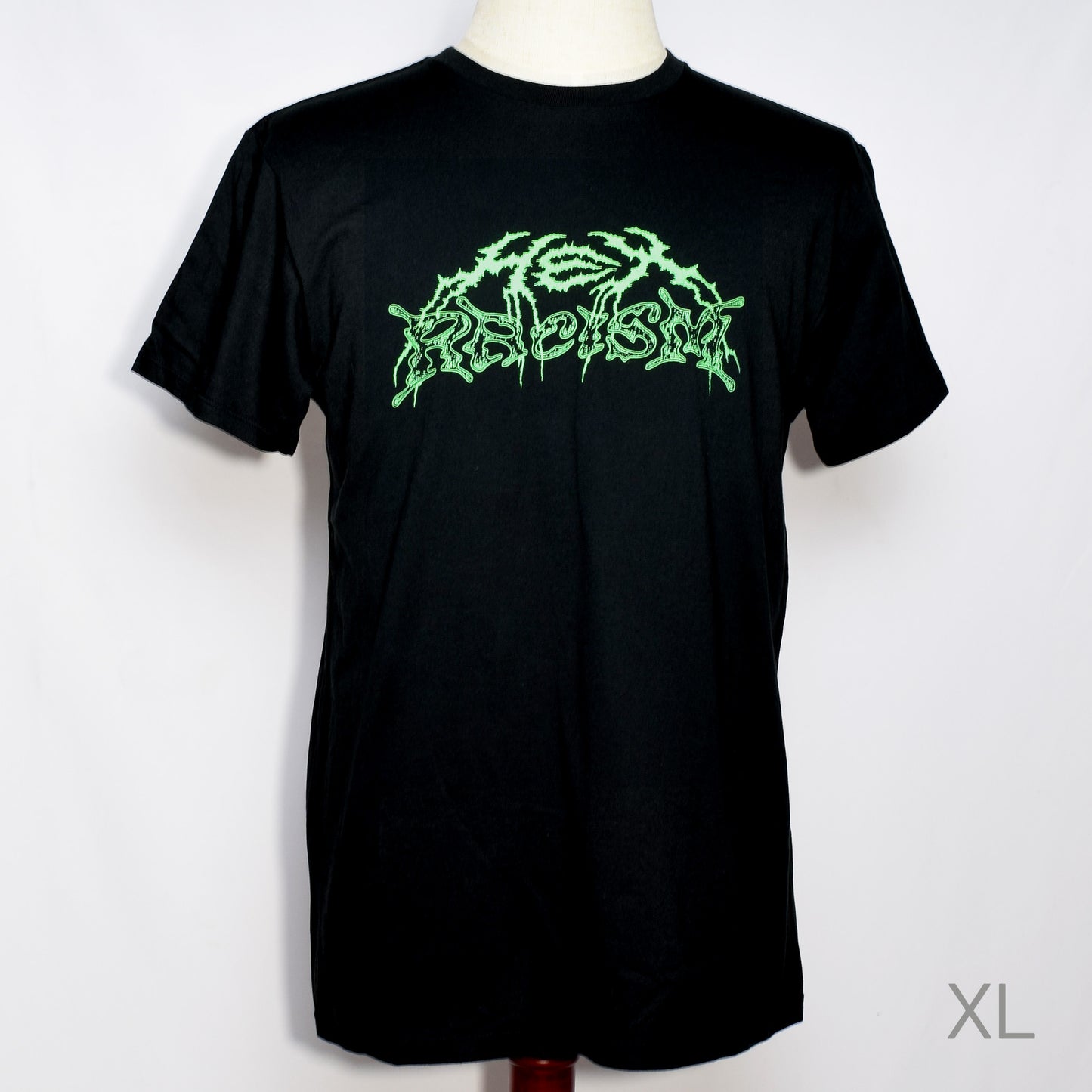 黒のTシャツにメタル風ロゴでHEX RACISM と蛍光グリーンでプリントされている。後ろは祝共生の文字と悪魔、魔女、髭の長い男性の魔女が笑顔でダンスしているイラストがグレーでプリントされている。