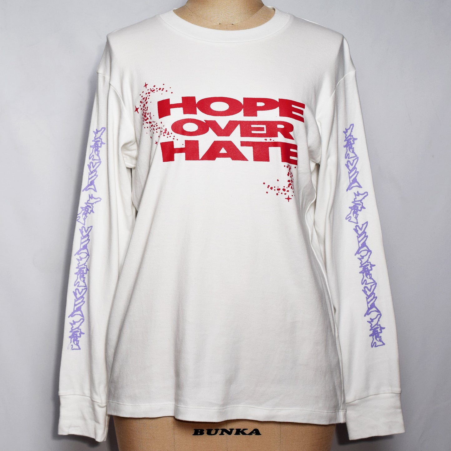 ロングスリーブTシャツ(白色)にHOPE OVER HATEの赤色のプリントと、袖に薄紫の途切れた有刺鉄線のプリント。